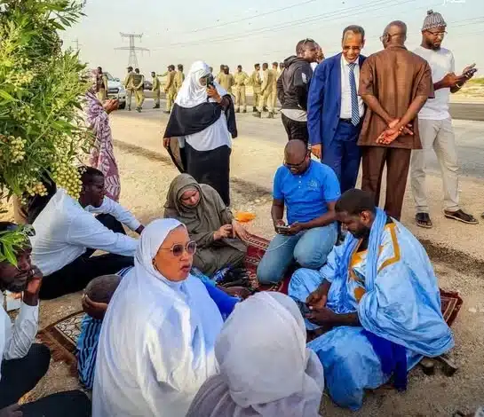 Biram Dah Abeid assis paisiblement sous un arbre, entouré de militants, tandis que des forces de l’ordre se tiennent à distance en arrière-plan.