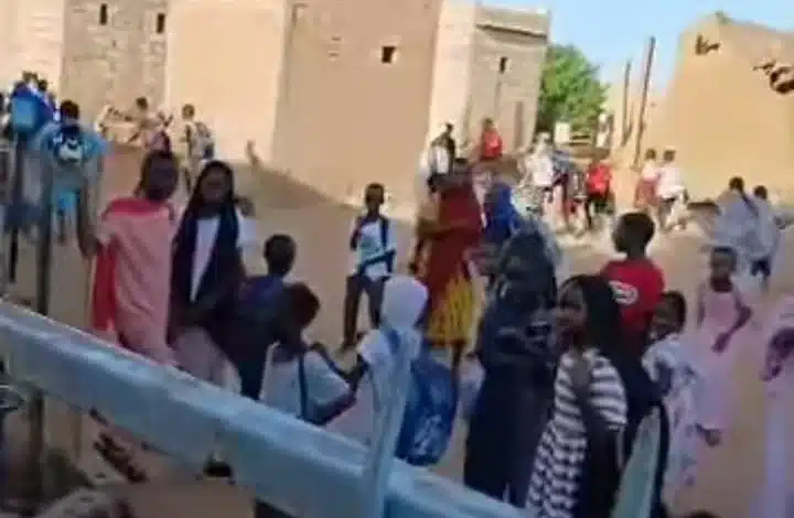 Des élèves mauritaniens en tenue scolaire discutent devant une école, illustrant le débat sur l’uniforme obligatoire.