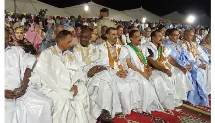 « Participants assis lors de la cérémonie d’ouverture d’un festival culturel mauritanien en plein air, sous des tentes et éclairages nocturnes. »