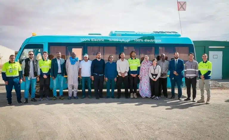 Groupe de journalistes et responsables de Kinross Tasiast posant devant un bus bleu 100 % électrique lors d’une visite du site minier.