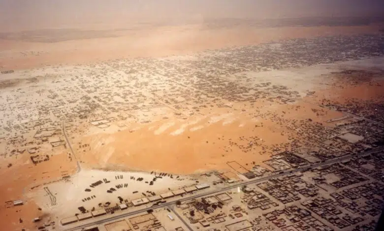 Développement en Mauritanie : Pourquoi un tel retard sur ses voisins ? 1 Une vue aérienne imprenable de Nouakchott, la capitale de la Mauritanie. L'image capture le tissu urbain complexe de la ville, montrant un mélange de quartiers résidentiels denses, de mosquées aux minarets distinctifs, et de bâtiments administratifs plus modernes. On distingue les principales artères routières traversant la ville, ainsi que la proximité du désert du Sahara, dont les dunes dorées bordent les limites de l'urbanisation, soulignant le défi de l'expansion de la ville. Au loin, on aperçoit également la côte atlantique et la zone portuaire, éléments clés de l'économie mauritanienne.