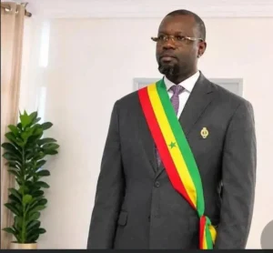 Sénégal : Ousmane Sonko élu président de l'Assemblée nationale 2 Portrait officiel d'Ousmane Sonko, président du Sénégal, en costume charcoal, portant l'écharpe présidentielle aux couleurs nationales (vert, jaune, rouge avec l'étoile verte), avec une broche de l'ordre national et des lunettes.