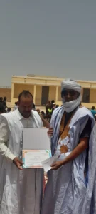 Nouakchott-Sud : L’école républicaine au cœur d’une journée pédagogique à El Mina 3 Un responsable éducatif remet une attestation de remerciement et une enveloppe à un enseignant en habit traditionnel lors de la journée pédagogique.