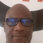 Dialogue politique en Mauritanie : Unir le peuple | Gourmo Lô 2 Portrait serré de Gourmo Abdoul Lô, professeur de droit public et homme politique mauritanien, portant des lunettes de vue, sur un fond blanc et rouge.