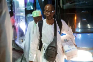 Les pèlerins du Groupe SNIM de retour à Nouakchott 4 Un pèlerin du groupe SNIM portant des lunettes et un colis descendant du bus à Nouakchott.