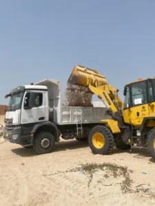 Environnement : la SNIM et les associations locales s’unissent pour assainir le littoral de Cansado 4 Une chargeuse Komatsu jaune déverse des déchets dans le plateau d'un camion-benne blanc aux couleurs de la SNIM.